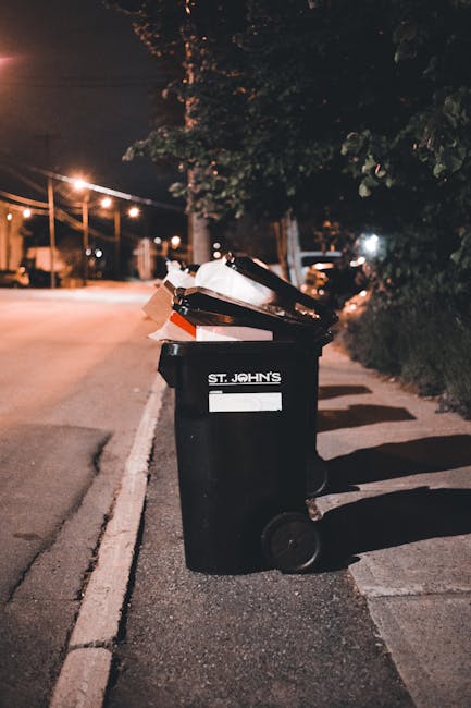 The image depicts a large outdoor area filled with miscellaneous household rubbish and discarded items, including a small red plastic toy car situated in the foreground. The toy car, made of painted p